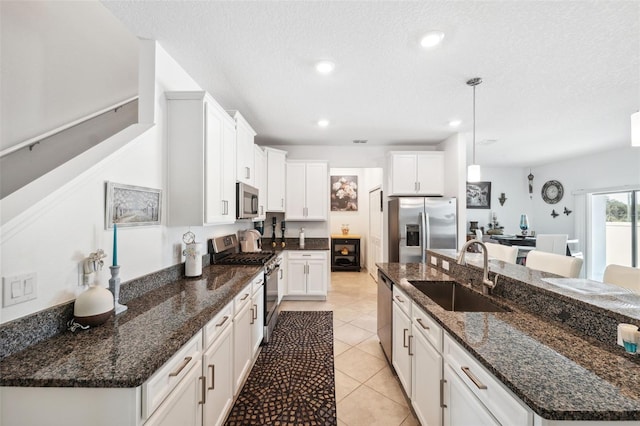 kitchen with appliances with stainless steel finishes, a kitchen island with sink, hanging light fixtures, sink, and white cabinets