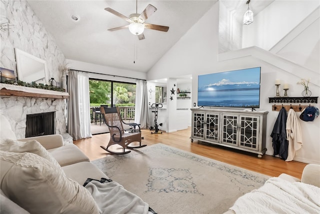 living room featuring a stone fireplace, ceiling fan, hardwood / wood-style floors, and high vaulted ceiling