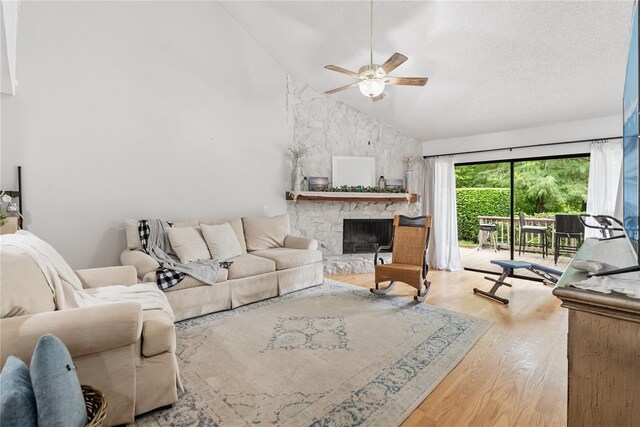 living room featuring a fireplace, light hardwood / wood-style flooring, ceiling fan, high vaulted ceiling, and a textured ceiling