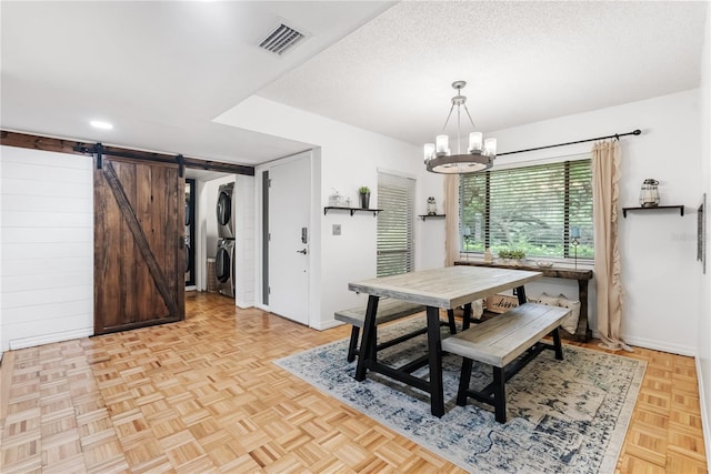 dining room with a barn door, a chandelier, stacked washer and dryer, light parquet floors, and a textured ceiling