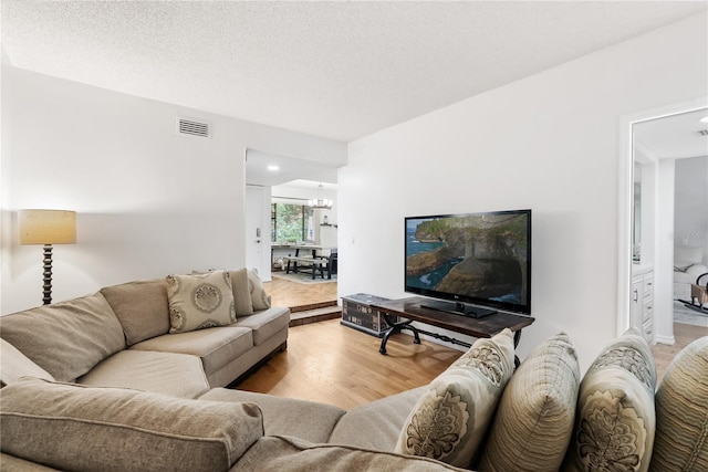 living room with a textured ceiling, light wood-type flooring, and a chandelier