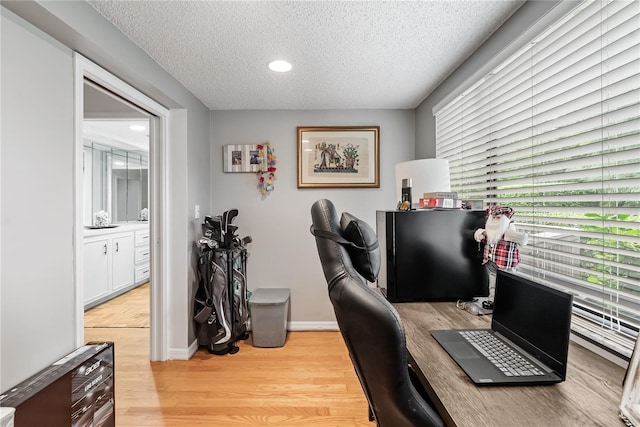 office space with light wood-type flooring, baseboards, and a textured ceiling