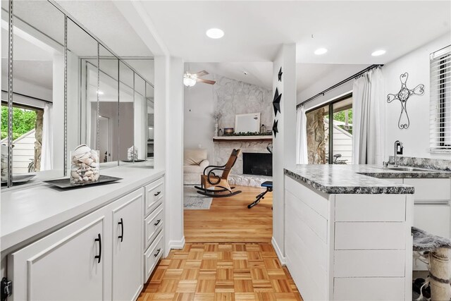 kitchen with vaulted ceiling, a stone fireplace, sink, ceiling fan, and white cabinets