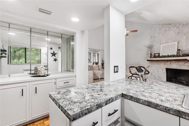 kitchen with light parquet flooring, ceiling fan, white cabinets, and a stone fireplace