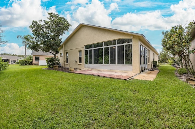 back of property featuring stucco siding, a lawn, and a sunroom