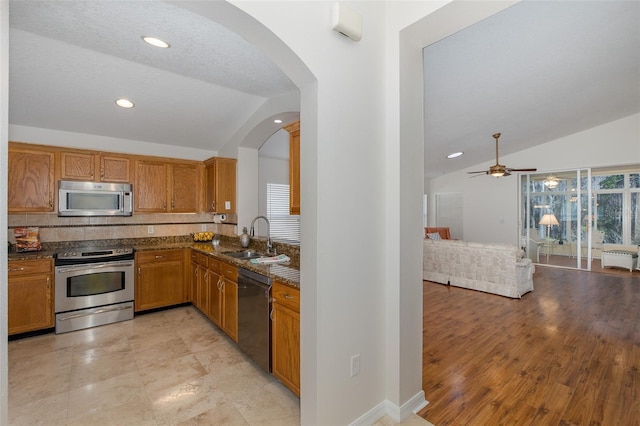 kitchen with a sink, lofted ceiling, brown cabinetry, and stainless steel appliances