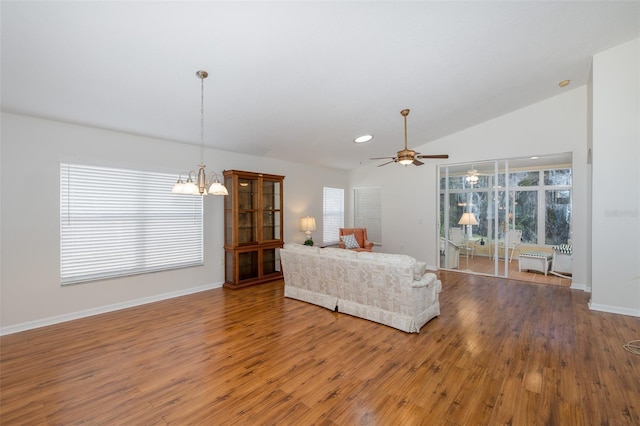 unfurnished living room featuring ceiling fan with notable chandelier, vaulted ceiling, wood finished floors, and baseboards