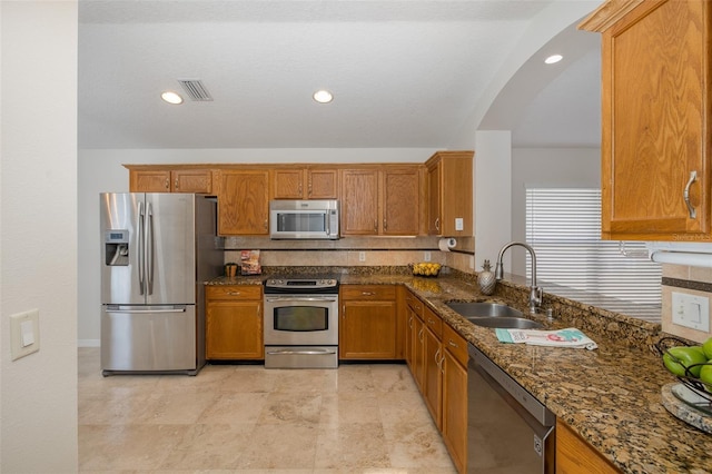 kitchen featuring brown cabinetry, visible vents, dark stone counters, a sink, and appliances with stainless steel finishes