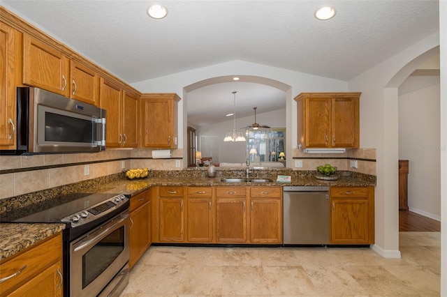 kitchen with vaulted ceiling, appliances with stainless steel finishes, sink, decorative backsplash, and dark stone counters