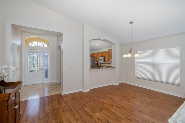 entryway featuring a chandelier, arched walkways, baseboards, and dark wood finished floors