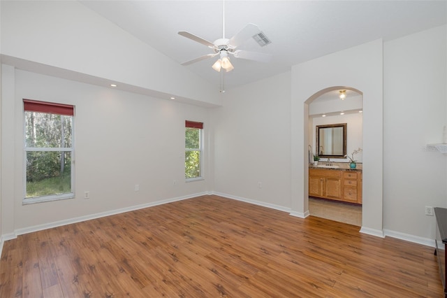 empty room featuring ceiling fan, a healthy amount of sunlight, vaulted ceiling, and light wood-type flooring