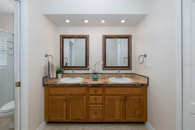 bathroom featuring walk in shower, double vanity, toilet, and a sink