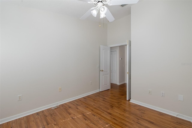 empty room with a towering ceiling, ceiling fan, baseboards, and wood finished floors