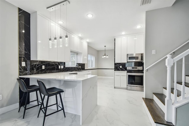 kitchen featuring kitchen peninsula, sink, hanging light fixtures, stainless steel appliances, and white cabinets