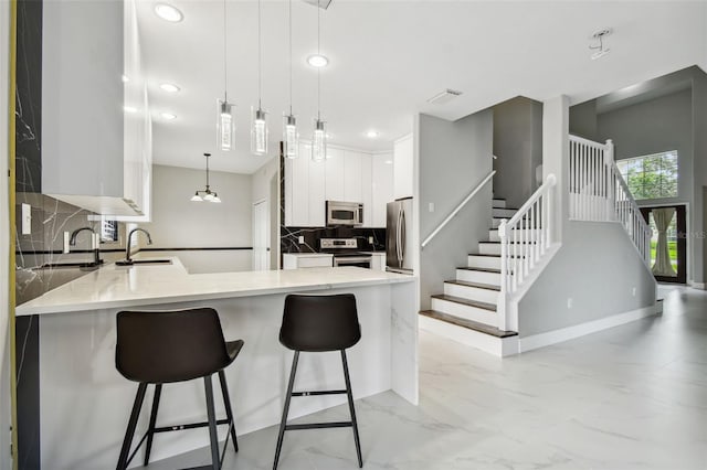 kitchen with kitchen peninsula, appliances with stainless steel finishes, pendant lighting, and white cabinetry