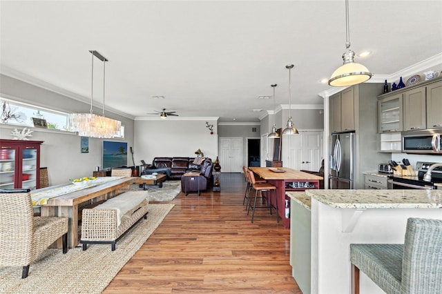 kitchen with gray cabinetry, stainless steel appliances, light wood-type flooring, decorative light fixtures, and ornamental molding