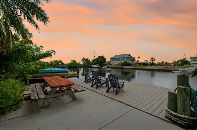 patio terrace at dusk featuring a boat dock and a water view