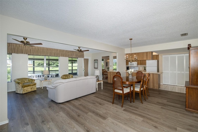 dining area featuring dark wood-type flooring, a textured ceiling, and ceiling fan with notable chandelier