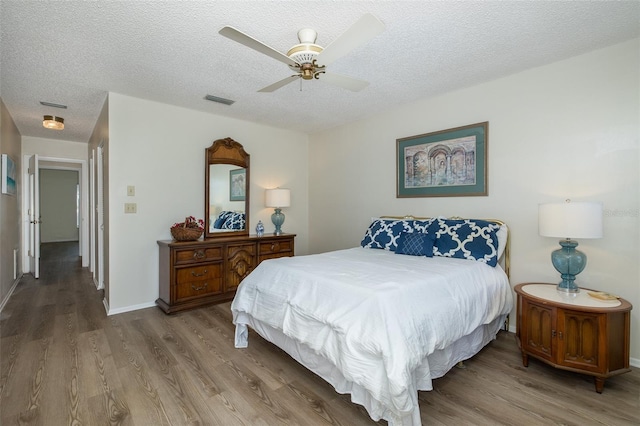 bedroom with a textured ceiling, wood-type flooring, and ceiling fan