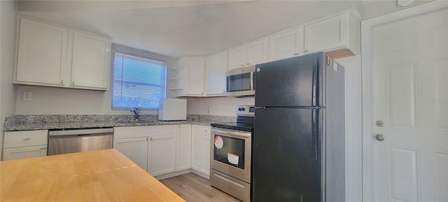 kitchen with light stone countertops, sink, stainless steel appliances, white cabinets, and light wood-type flooring