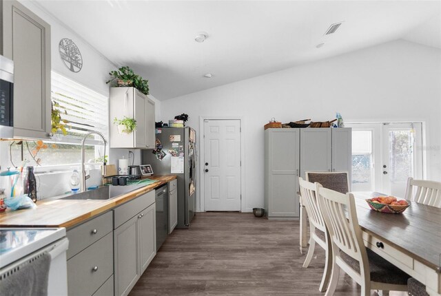 kitchen featuring wooden counters, sink, vaulted ceiling, hardwood / wood-style flooring, and stainless steel dishwasher