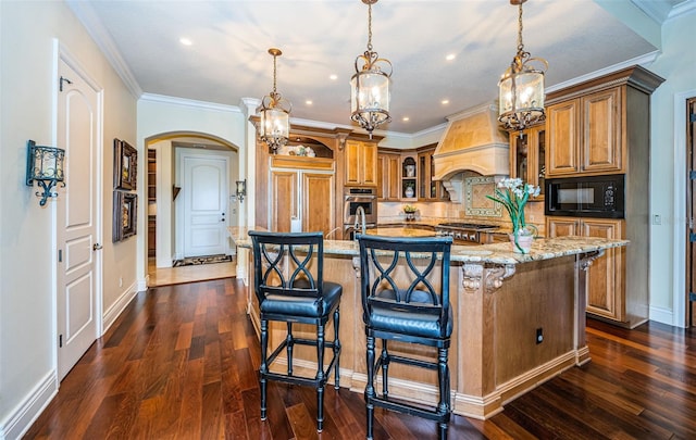 kitchen featuring light stone counters, custom exhaust hood, dark wood-type flooring, built in appliances, and a center island with sink