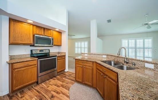 kitchen with sink, ceiling fan, appliances with stainless steel finishes, light stone counters, and light wood-type flooring