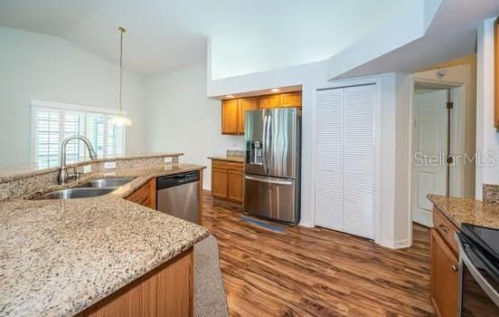 kitchen featuring lofted ceiling, sink, decorative light fixtures, stainless steel appliances, and light stone countertops