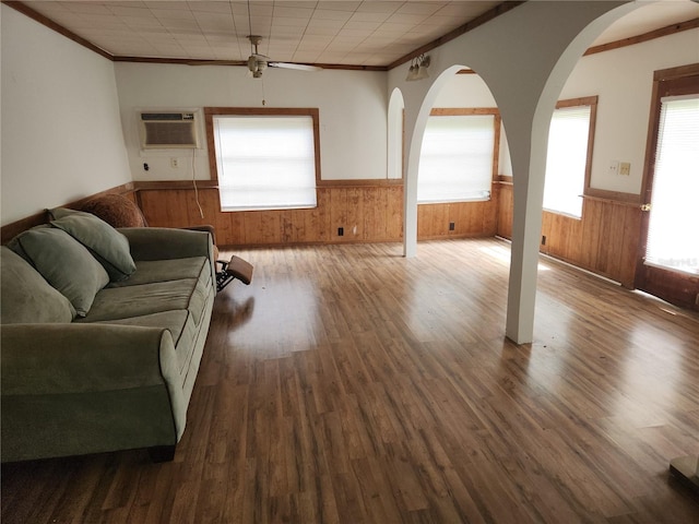 living room with wood-type flooring, crown molding, ceiling fan, a wall unit AC, and wooden walls