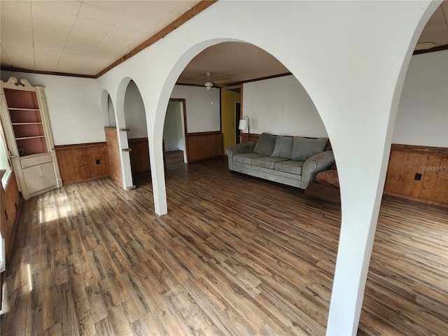 unfurnished living room with wooden walls, ceiling fan, dark wood-type flooring, and crown molding