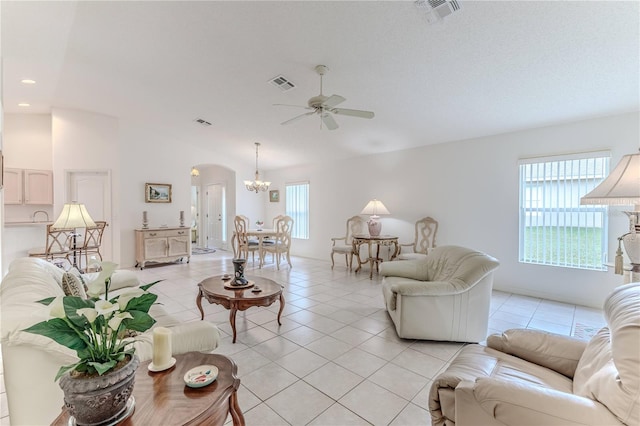 tiled living room featuring a healthy amount of sunlight, vaulted ceiling, and ceiling fan with notable chandelier