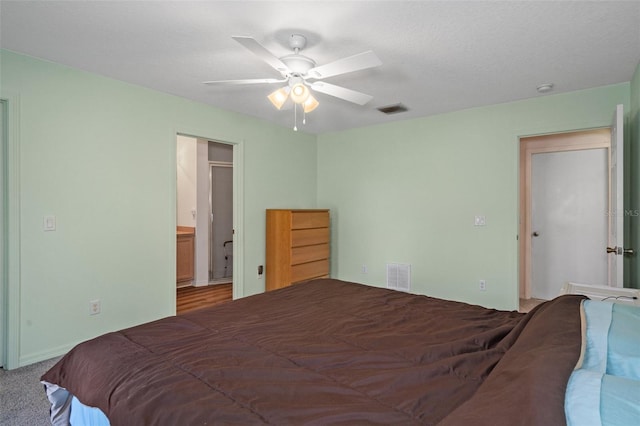 carpeted bedroom with a textured ceiling, ensuite bath, and ceiling fan