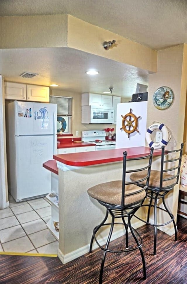 kitchen with a textured ceiling, a kitchen breakfast bar, white appliances, light hardwood / wood-style floors, and white cabinets