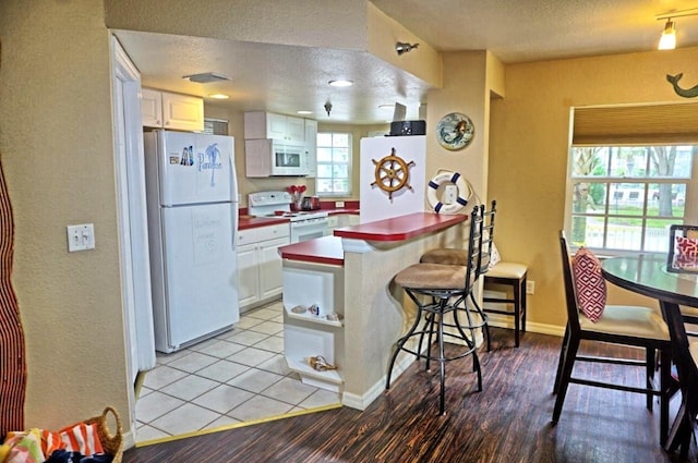 kitchen with visible vents, white appliances, a peninsula, a textured ceiling, and white cabinetry