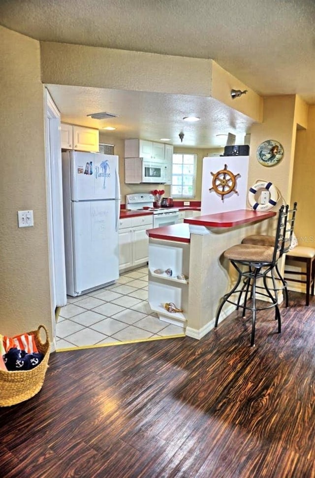 kitchen featuring light wood-type flooring, white appliances, a textured wall, a peninsula, and a textured ceiling