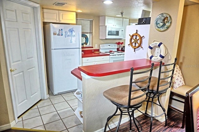 kitchen with white appliances, a kitchen bar, visible vents, light tile patterned flooring, and baseboards