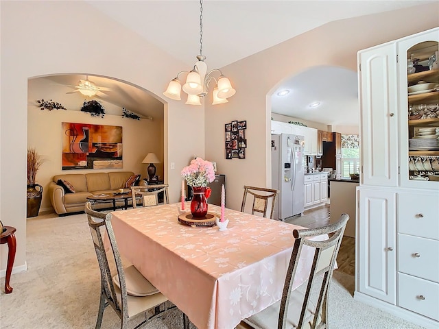 dining room featuring ceiling fan with notable chandelier, light colored carpet, and vaulted ceiling