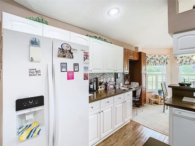 kitchen featuring white appliances, light hardwood / wood-style flooring, backsplash, a textured ceiling, and white cabinets