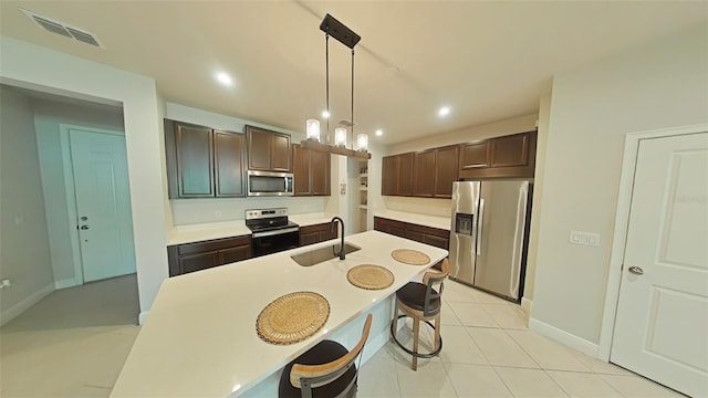 kitchen with dark brown cabinetry, pendant lighting, light tile patterned flooring, sink, and stainless steel appliances