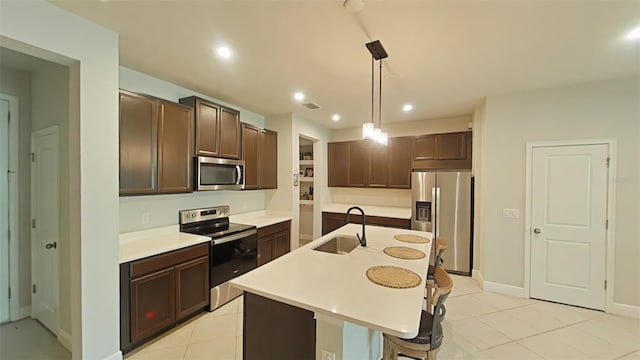 kitchen with pendant lighting, light tile patterned flooring, sink, stainless steel appliances, and a center island with sink