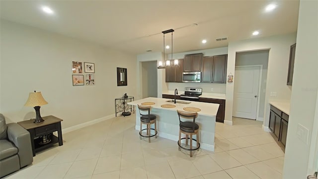 kitchen featuring sink, an island with sink, appliances with stainless steel finishes, decorative light fixtures, and dark brown cabinetry