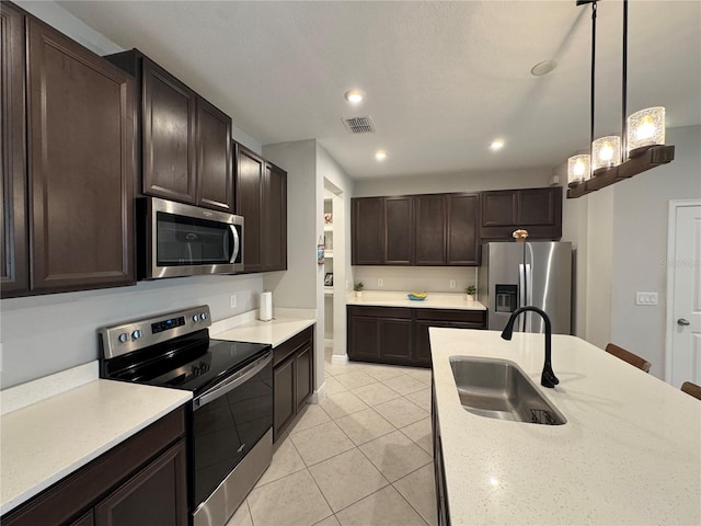 kitchen featuring light tile patterned floors, dark brown cabinetry, a sink, appliances with stainless steel finishes, and pendant lighting