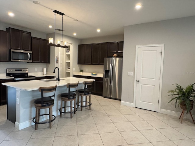 kitchen featuring pendant lighting, light countertops, appliances with stainless steel finishes, a kitchen island with sink, and a sink