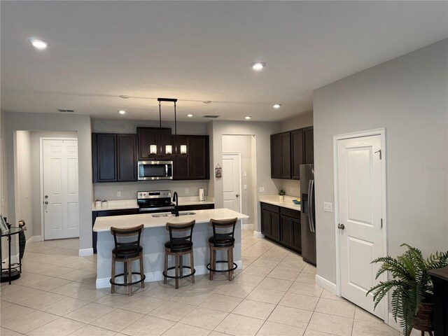 kitchen with decorative light fixtures, a center island with sink, light countertops, appliances with stainless steel finishes, and dark brown cabinets