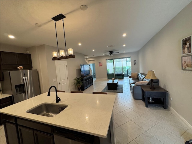 kitchen with a center island with sink, light stone counters, hanging light fixtures, stainless steel appliances, and a sink