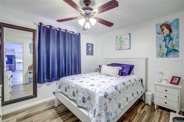 bedroom with wood-type flooring, ceiling fan, and stainless steel refrigerator