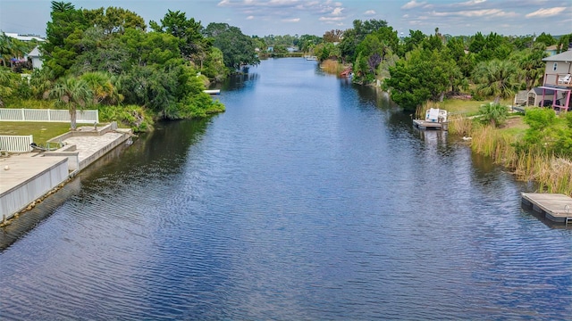water view with fence, a tree filled landscape, a boat ramp, and a boat dock