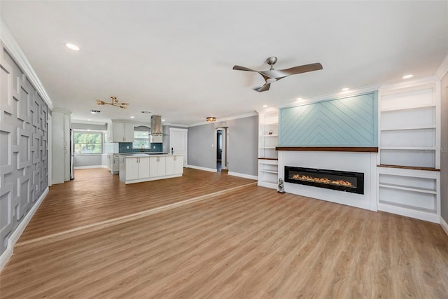 unfurnished living room with crown molding, light hardwood / wood-style flooring, built in shelves, and ceiling fan