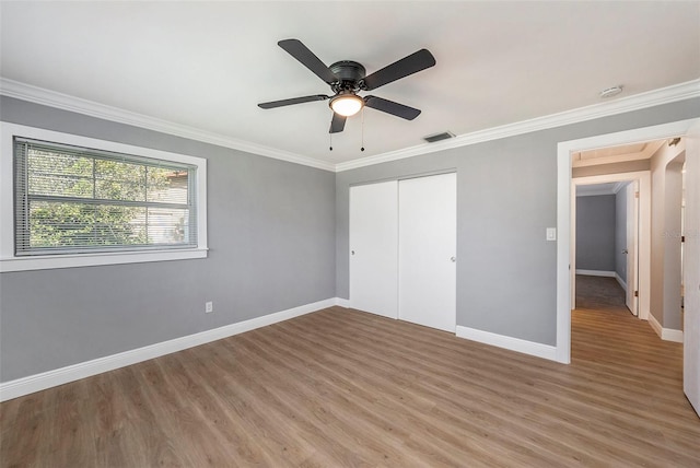 unfurnished bedroom featuring crown molding, light hardwood / wood-style floors, ceiling fan, and a closet