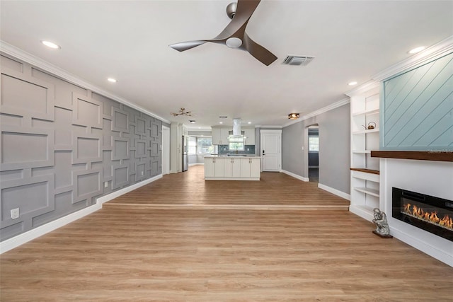 unfurnished living room with light wood-type flooring, ornamental molding, and ceiling fan